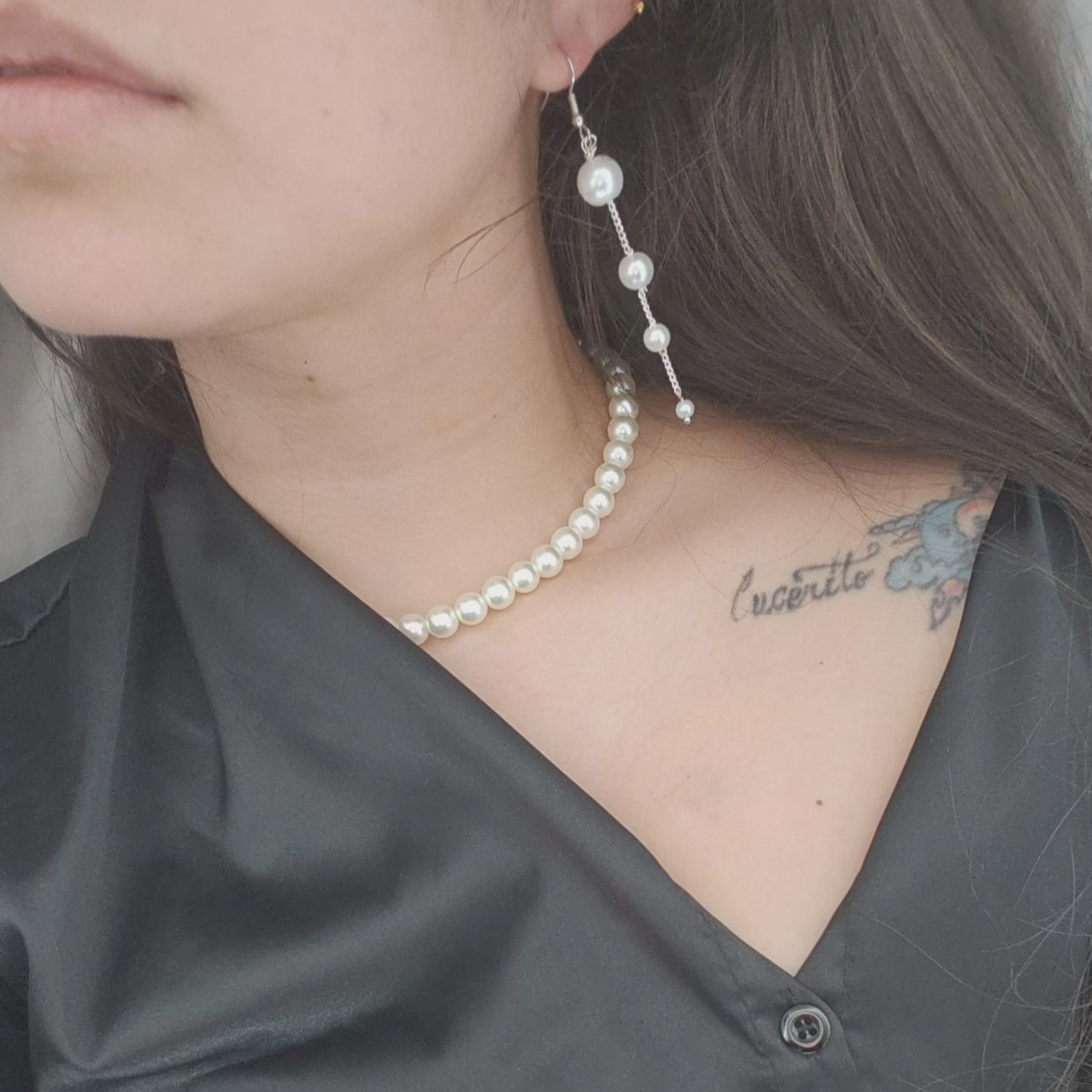 A person wearing a black shirt and white pearl earrings with a silver-plated chain.
